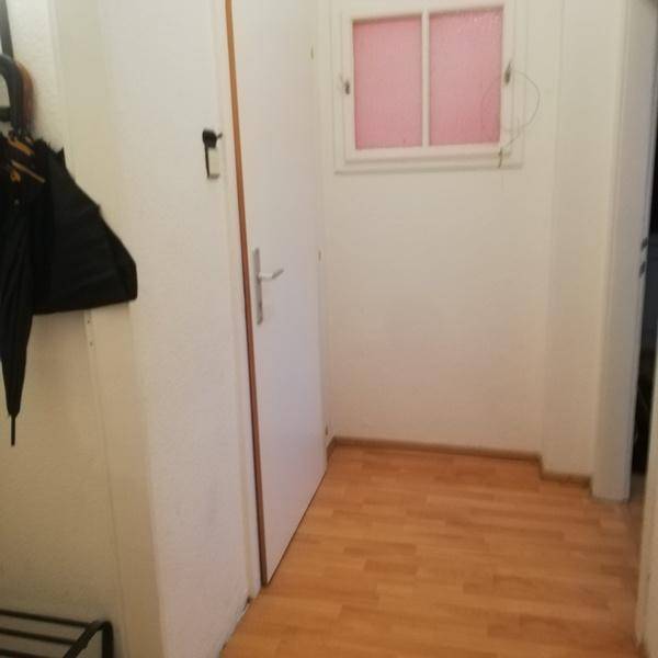 Heller Flur mit Holzfußboden und einem kleinen Fenster, das Tageslicht hereinlässt.