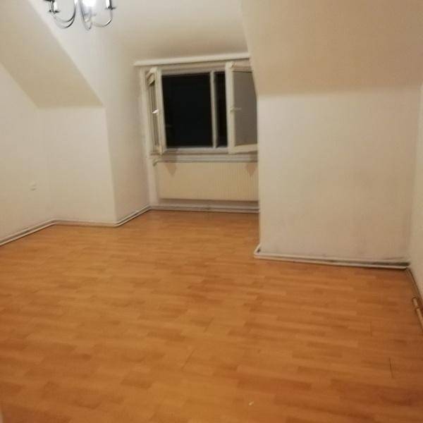 Leeres Zimmer im Dachgeschoss mit schrägen Wänden, Holzfußboden und einem Fenster.