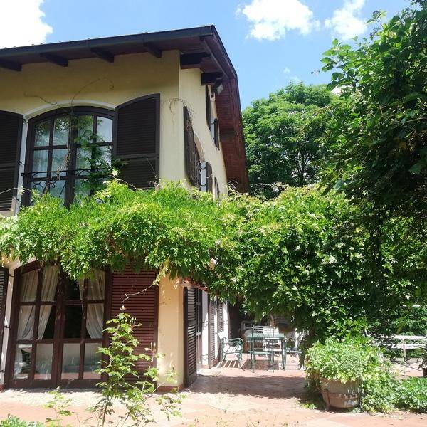 Seitlicher Blick auf das Haus mit üppiger Begrünung und einer überdachten Terrasse mit Sitzgelegenheiten.