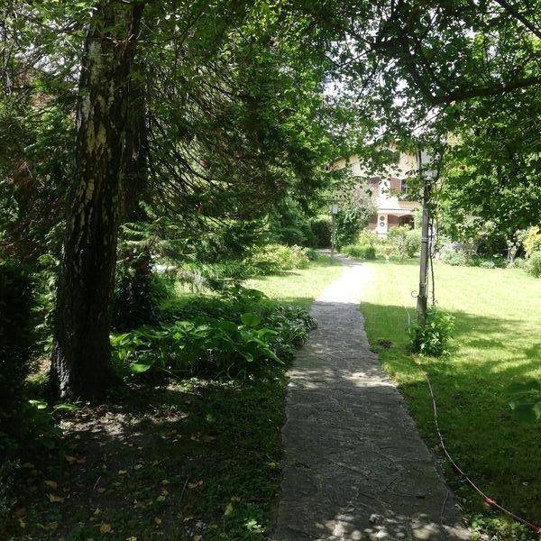 Langer Gartenweg führt durch eine grüne Allee zum Haupthaus im Hintergrund.