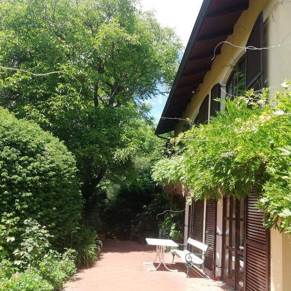 Idyllischer Gartenweg entlang der Hausfassade, umgeben von dichtem Grün und Bäumen.