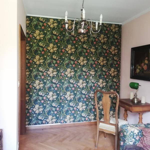 Raum mit auffälliger floraler Tapete, Parkettboden und klassischem Kronleuchter, ideal als Essbereich.