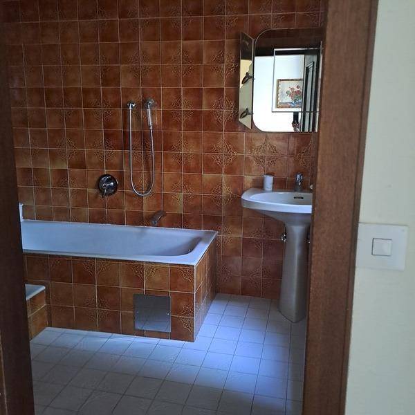 Badezimmer mit braunen Fliesen, Badewanne und Waschbecken, typisch für die 80er Jahre.