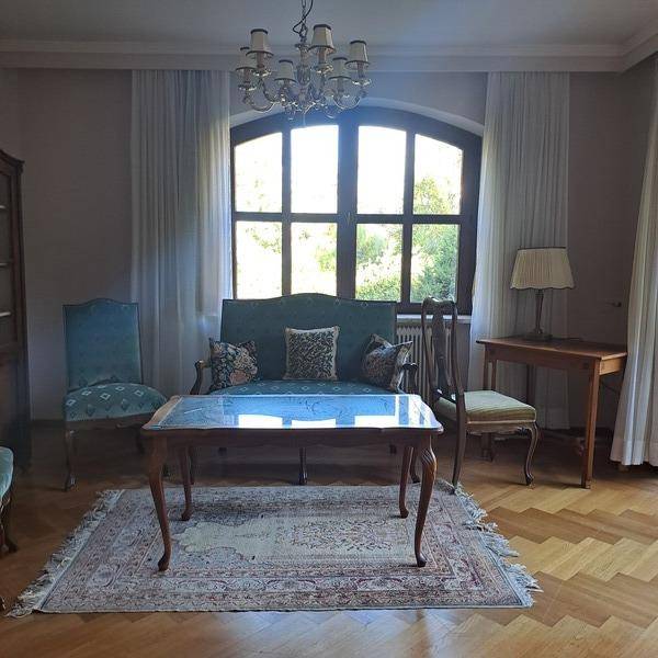 Klassisches Wohnzimmer mit Parkettboden, großem Bogenfenster und antiken Möbeln.