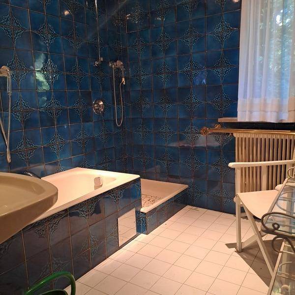 Badezimmer mit auffälligen blauen Fliesen, Badewanne und Duschbereich, sowie einem Fenster.