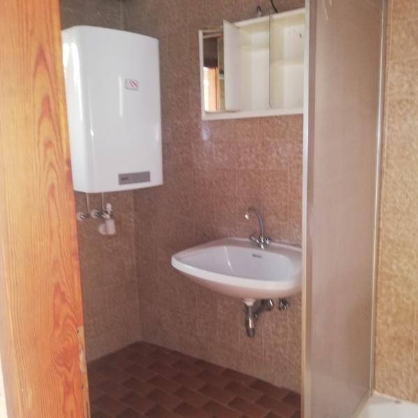 Badezimmer mit Warmwasserbereiter, Waschbecken und Duschbereich, alles gefliest.