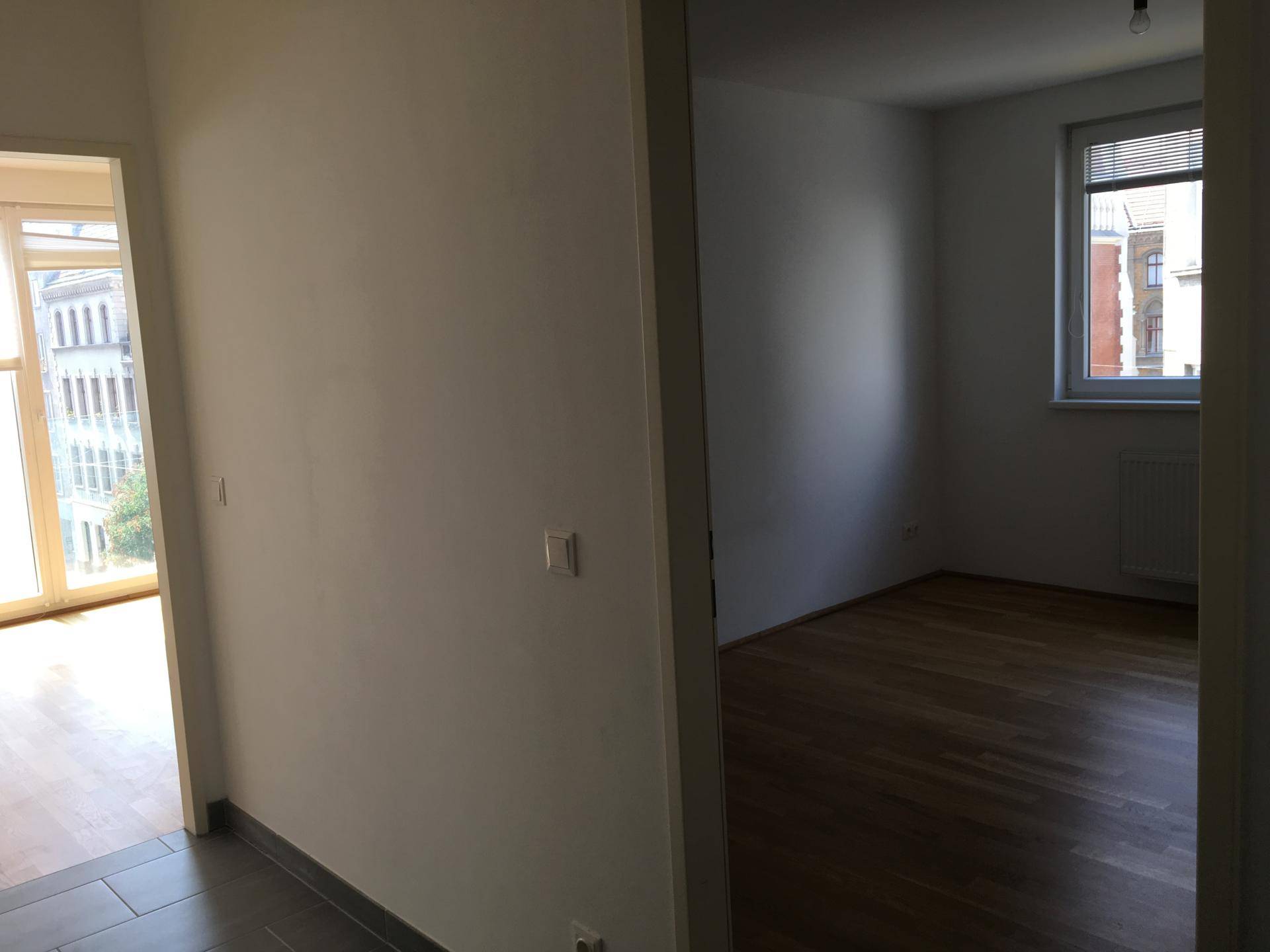 Blick von einem Flur in zwei separate Räume mit unterschiedlichen Bodenbelägen und Fenstern.