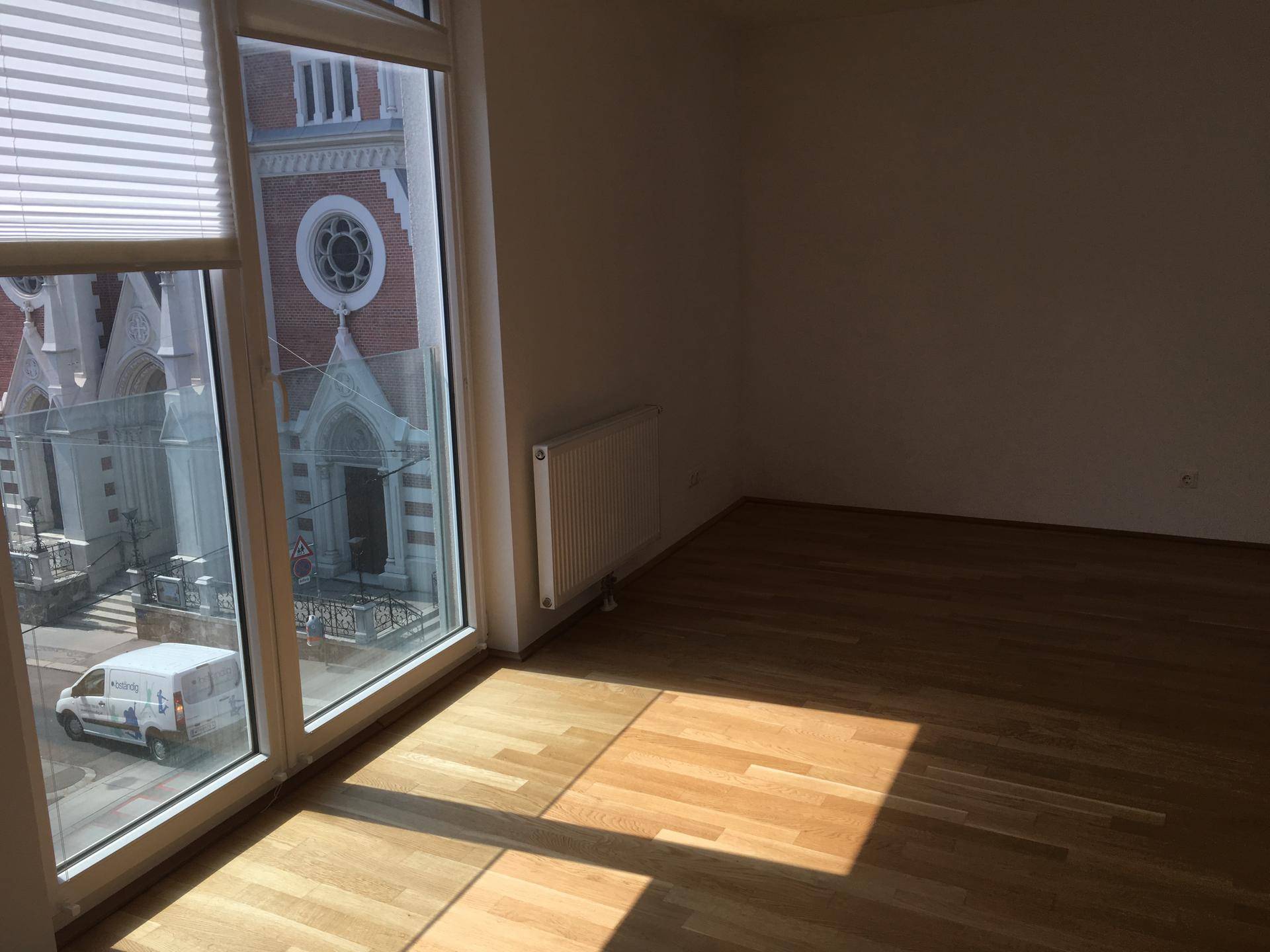 Helles Wohnzimmer mit Parkettboden und großen Fenstern, die einen Blick auf ein historisches Gebäude bieten.