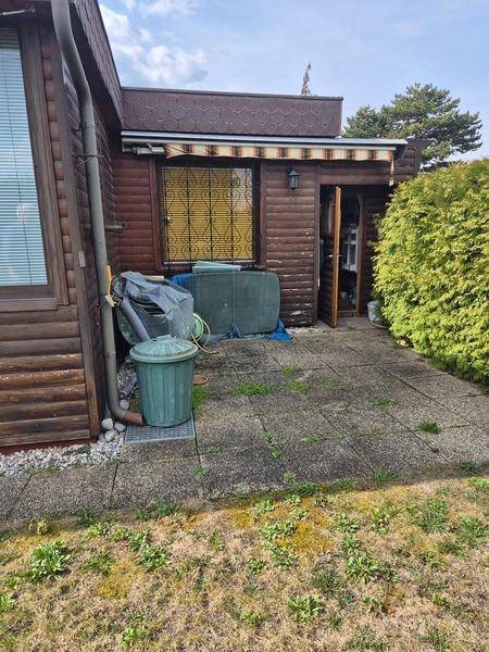 Gepflasterte Terrasse neben dem Haus mit Holzverkleidung und einem Mülleimer im Freien.