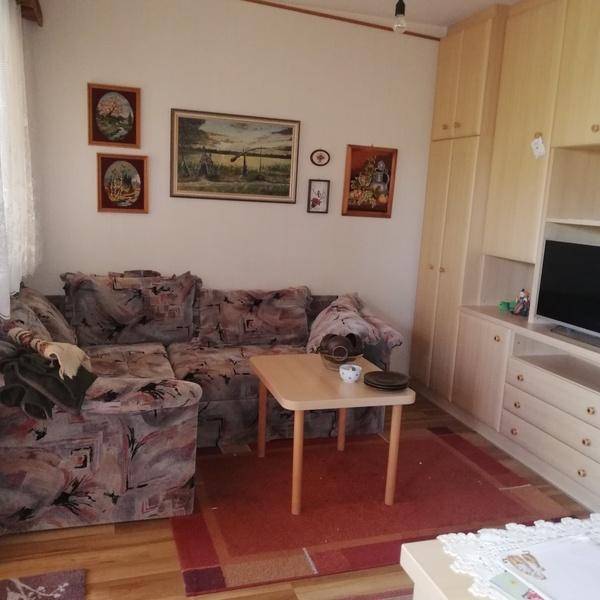 Wohnzimmer mit gemustertem Sofa, kleinem Couchtisch und einer hellen Schrankwand mit Fernseher.