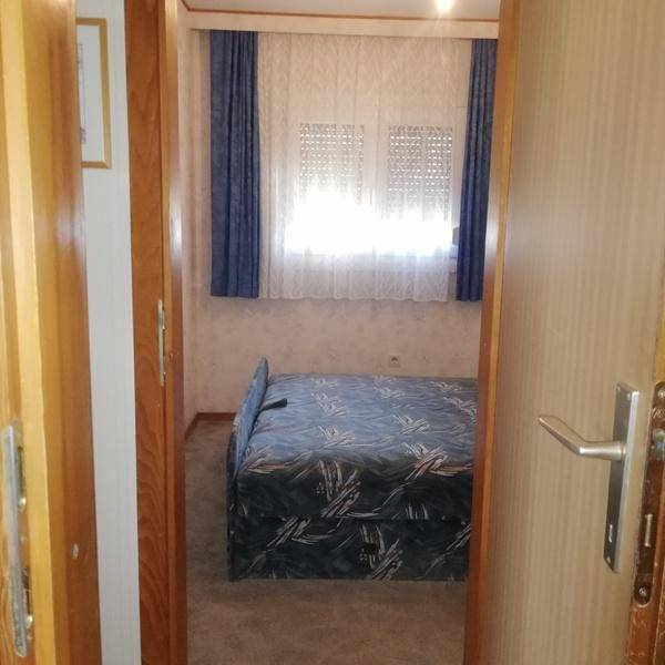Schlafzimmer mit blau gemustertem Bett und Fenster mit passenden Vorhängen, gesehen durch eine offene Tür.