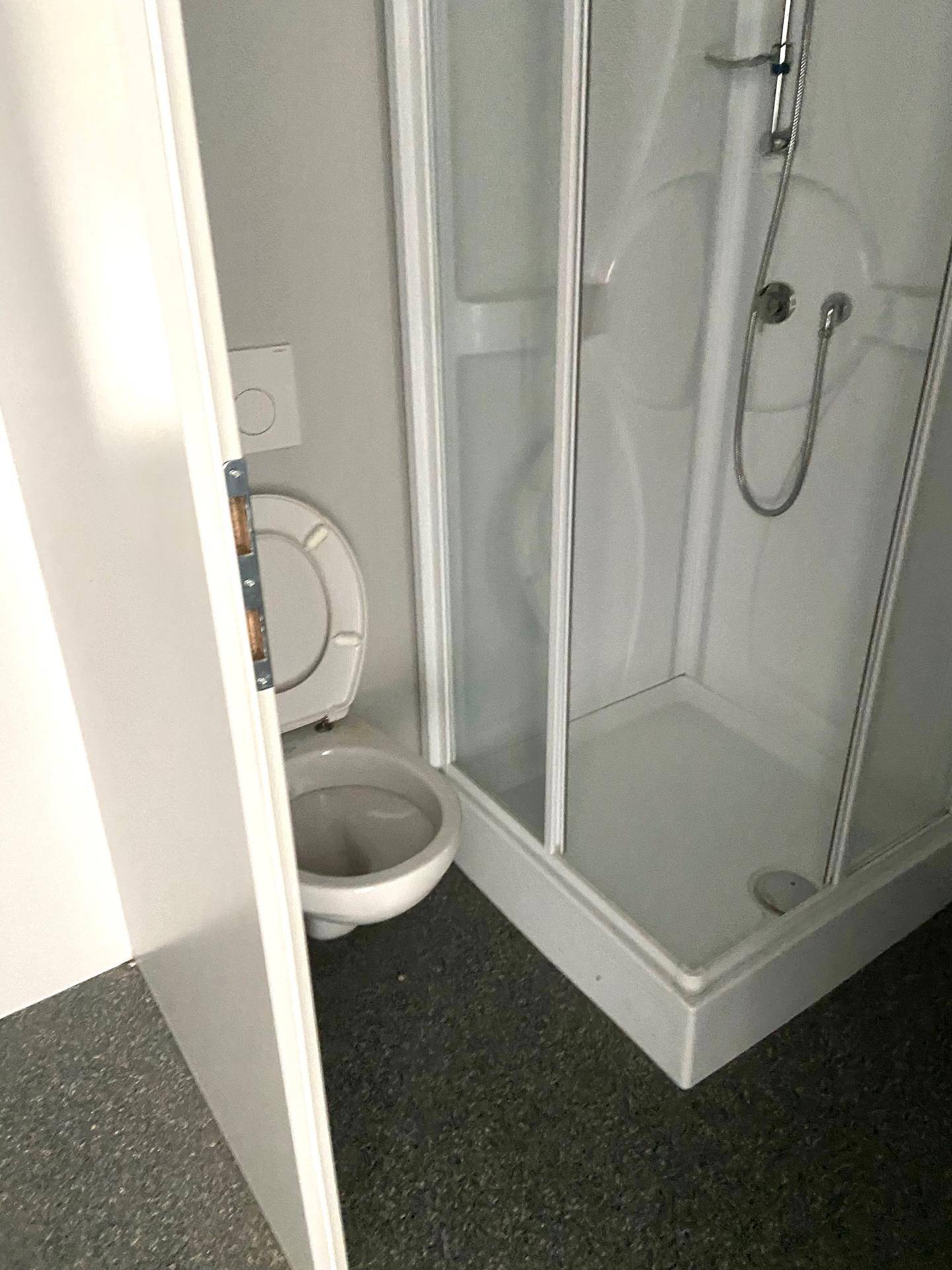 Kompaktes Badezimmer mit Toilette und Duschkabine, ausgestattet mit grauem Vinylboden.