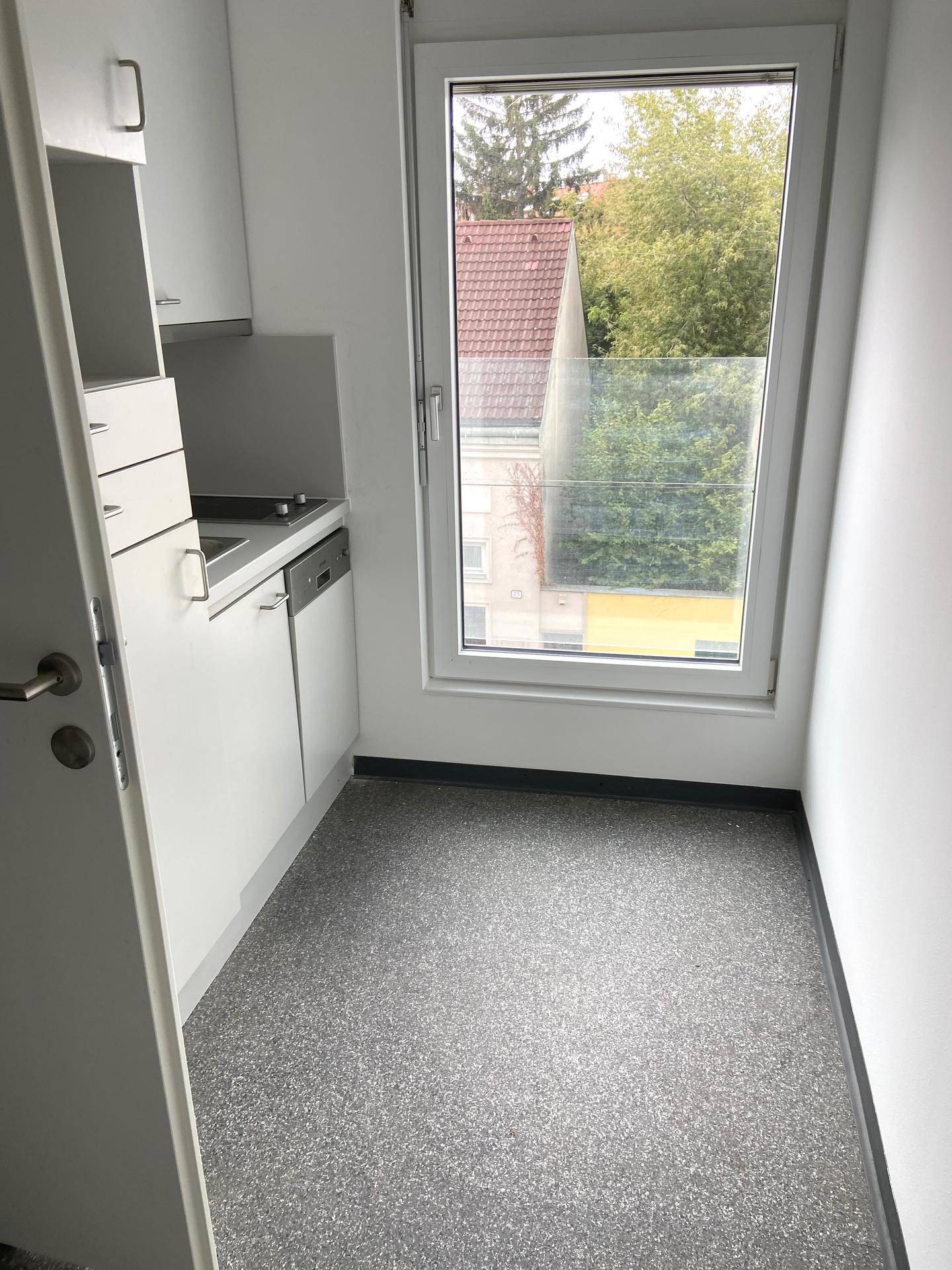 Kleine Küchenzeile in einem Raum mit Fenster, das einen Blick auf Bäume und Gebäude bietet.