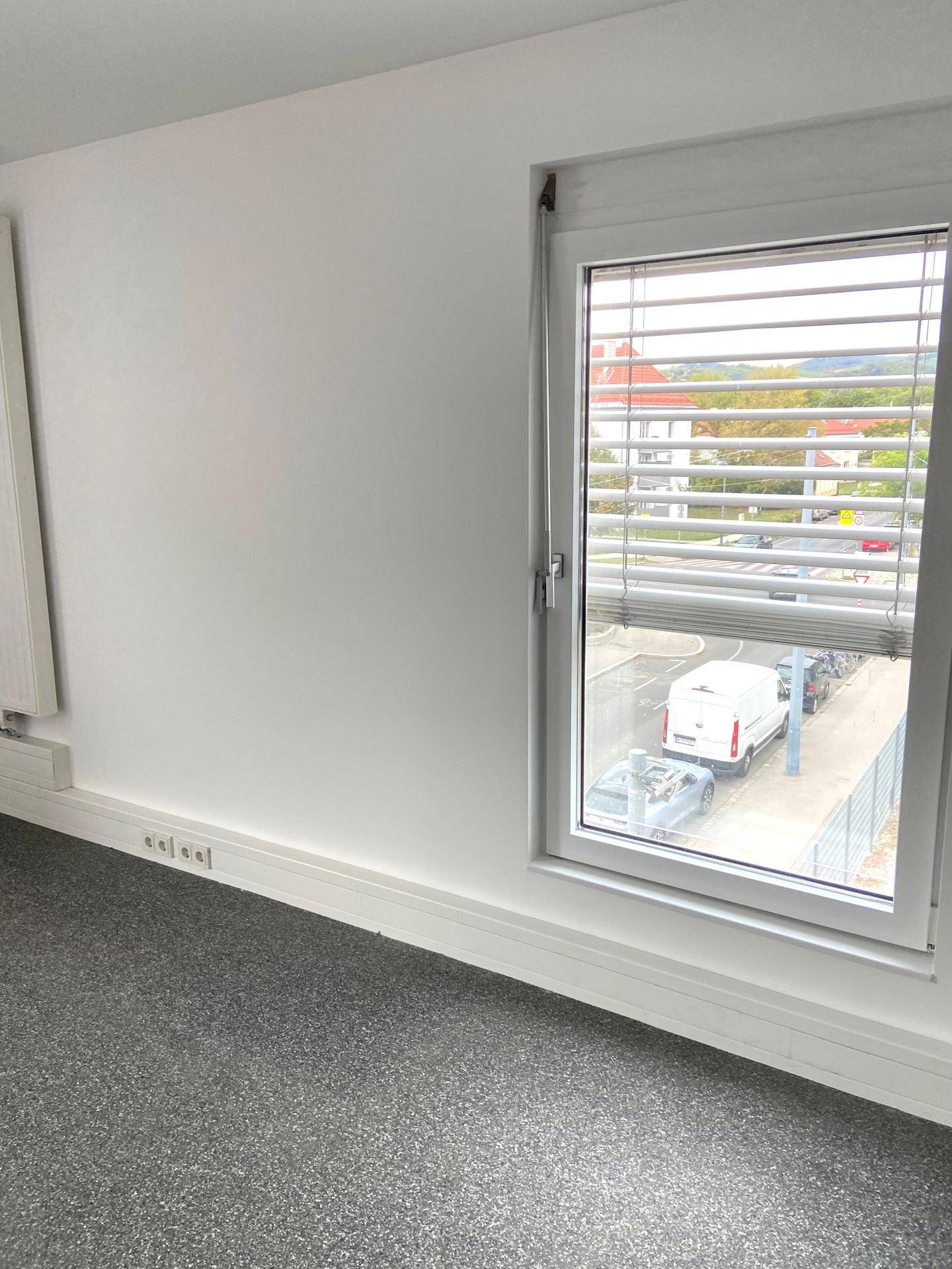 Heller, leerer Raum mit grauem Vinylboden und Fenster mit Blick auf die Straße.