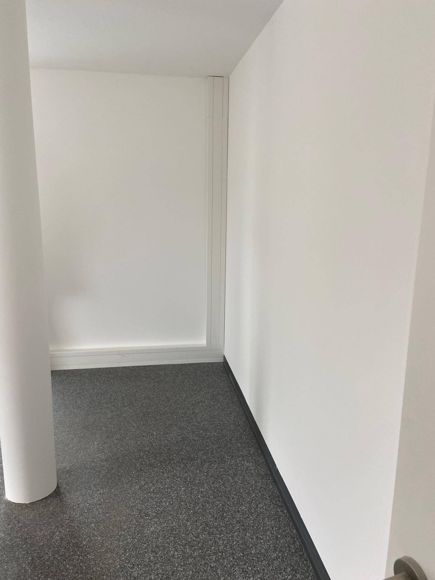 Ecke eines leeren Raumes mit weißen Wänden, einer Säule und grauem Vinylboden.