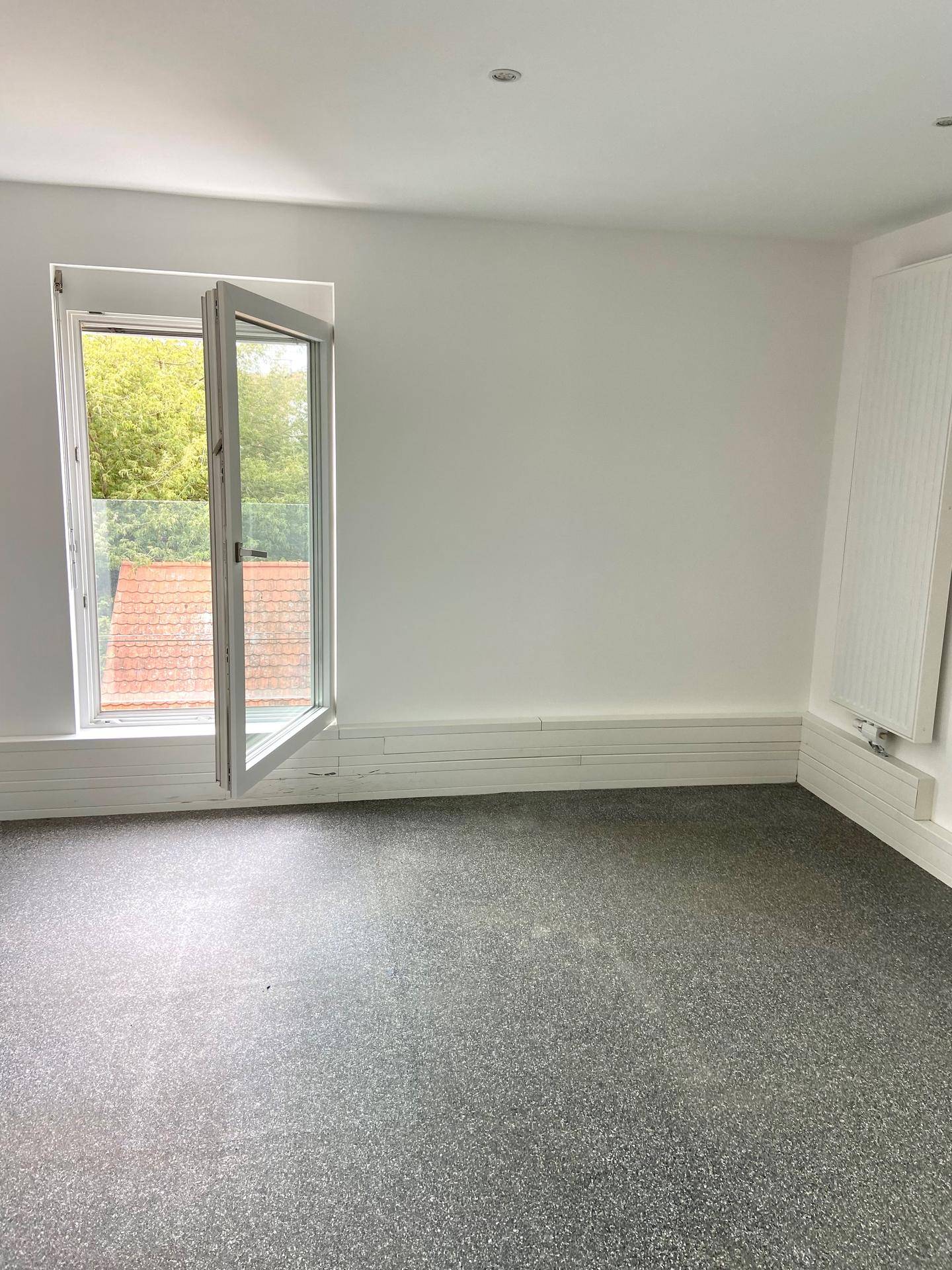 Geräumiger, leerer Raum mit weißen Wänden, grauem Vinylboden und geöffnetem Fenster.