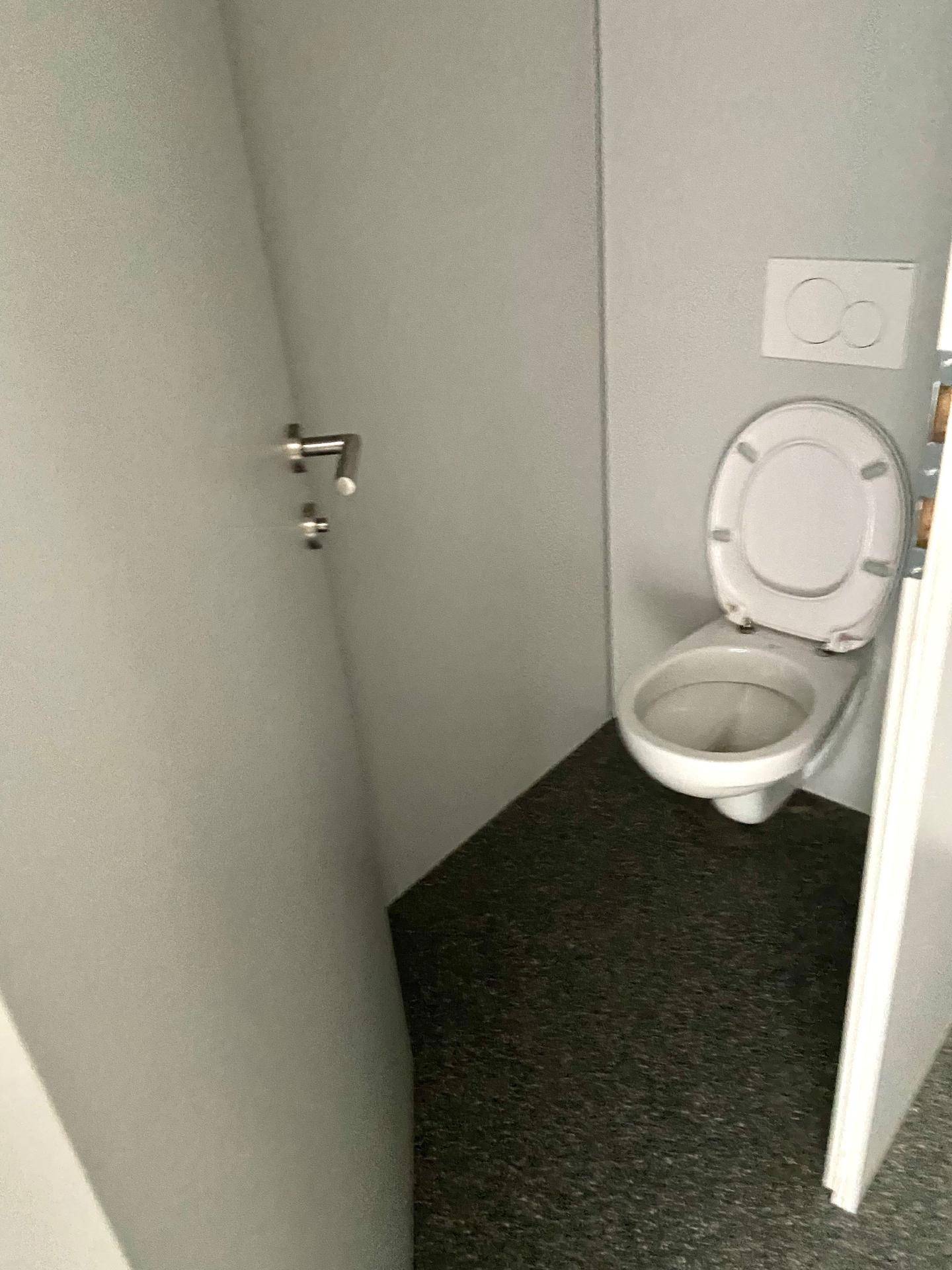Nahaufnahme einer Toilette in einem kleinen Badezimmer mit grauen Wänden und Boden.