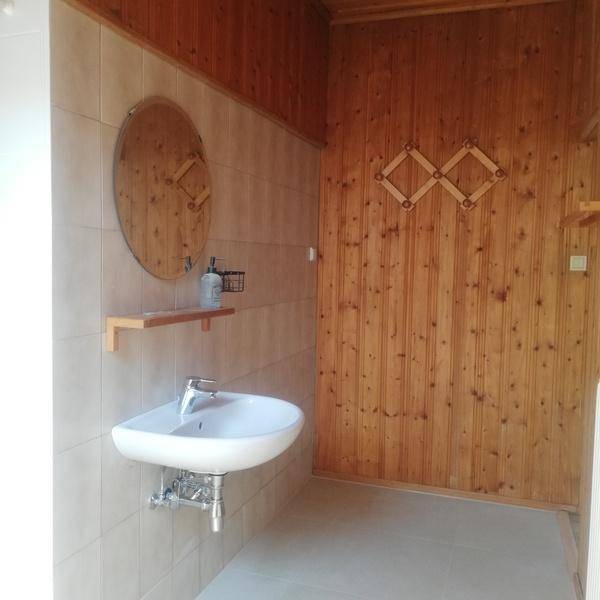 Badezimmer mit Waschbecken, rundem Spiegel und rustikaler Holzverkleidung an den Wänden.