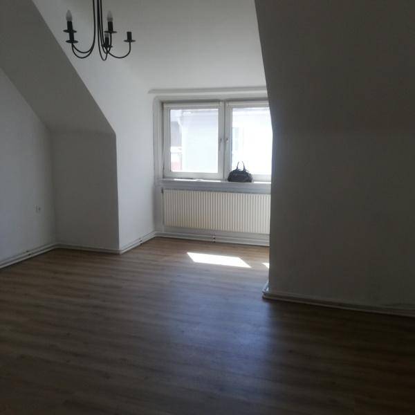 Helles Zimmer im Dachgeschoss mit Laminatboden, Dachschrägen und einem Fenster mit Ausblick.