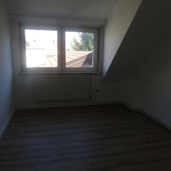 Leeres Zimmer im Dachgeschoss mit Laminatboden, Dachschrägen und einem Fenster.