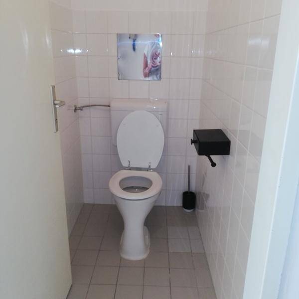 Separates WC mit weiß gefliesten Wänden, Toilette und kleinem Spiegel, sauber und funktional.