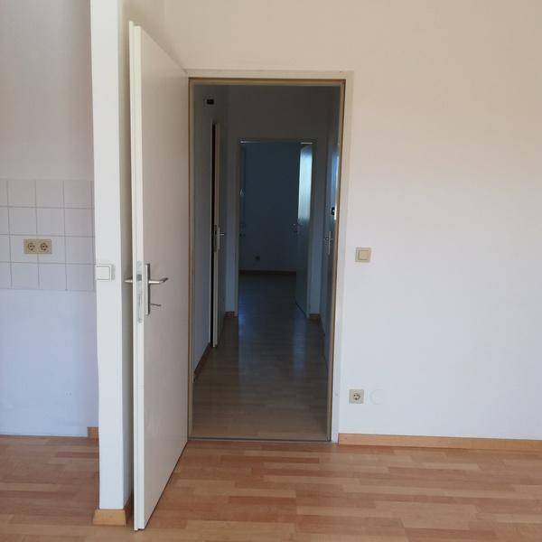 Blick durch eine offene Tür in einen hellen Flur mit Laminatboden und weiteren Zimmertüren.