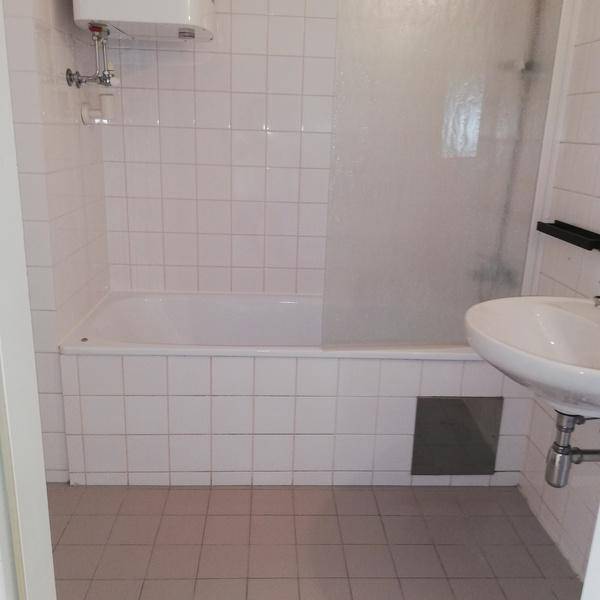 Badezimmer mit weiß gefliesten Wänden, Badewanne mit Duschabtrennung und Waschbecken.