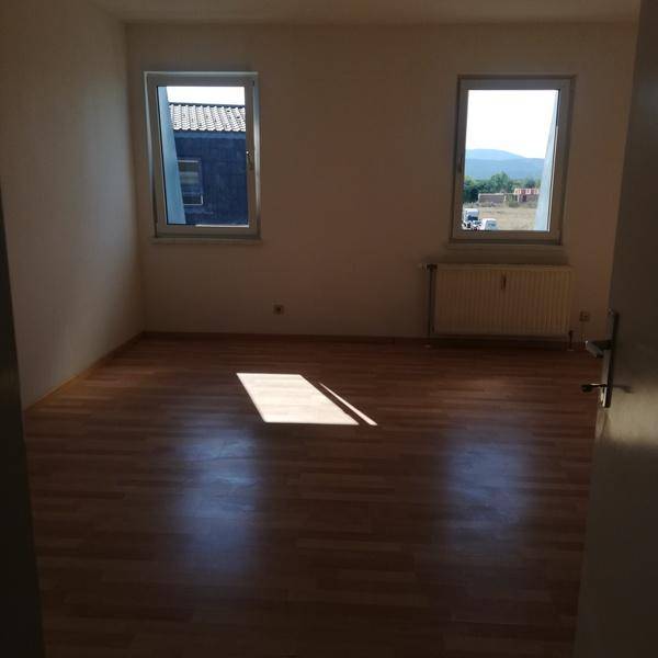 Helles Zimmer mit Laminatboden, zwei Fenstern und Heizkörper, bietet einen Blick ins Grüne.