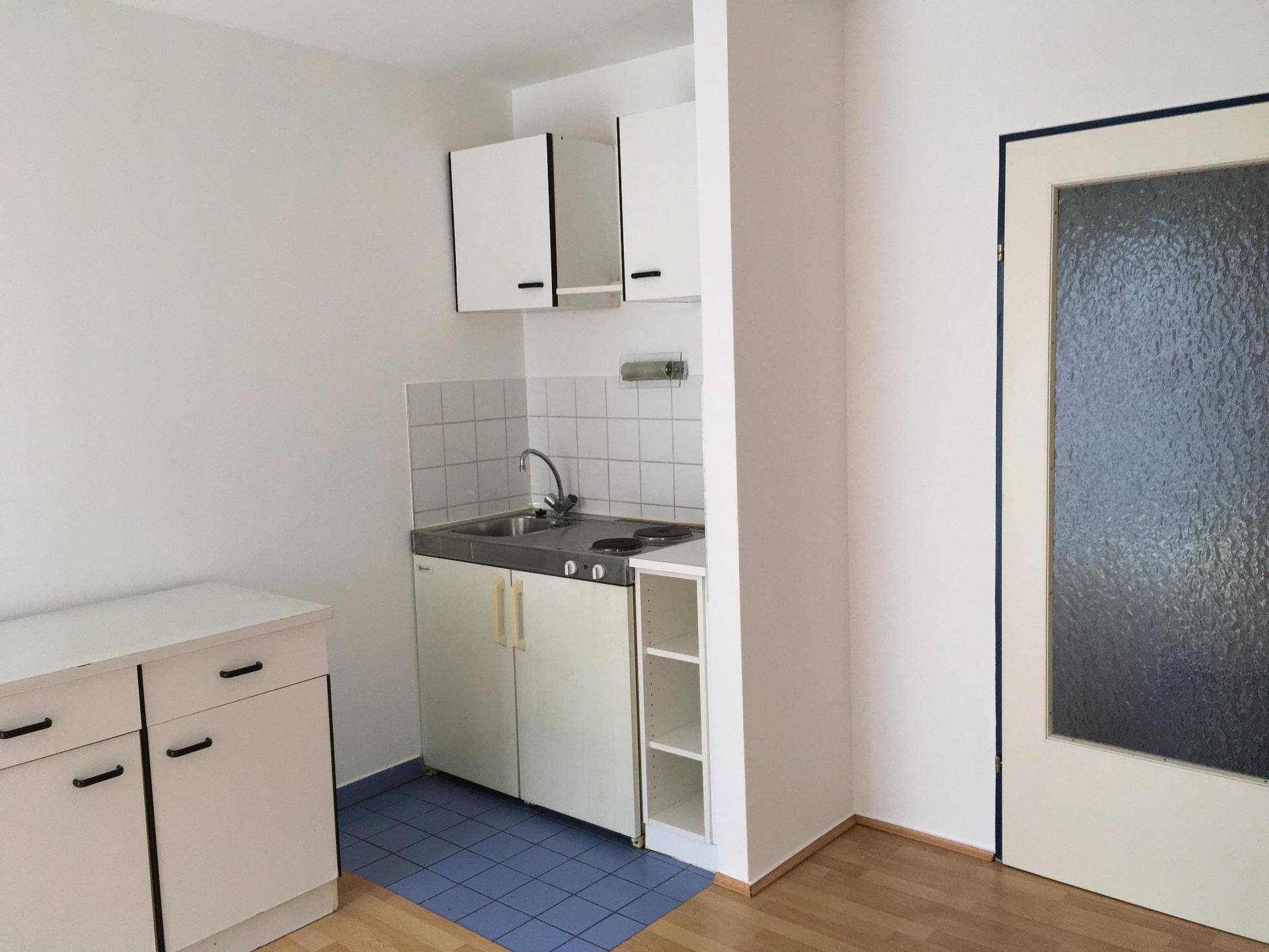 Funktionale Küchenzeile mit weißen Unterschränken, Kochfeld und Spüle, angrenzend an eine Tür mit Milchglas.