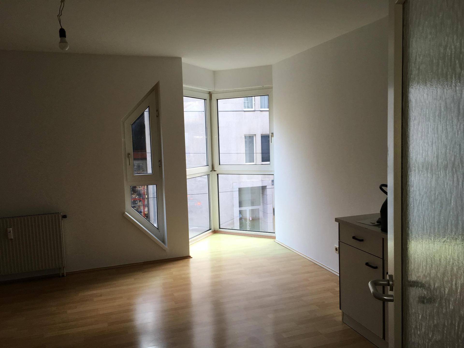 Lichtdurchfluteter Raum mit Parkettboden, Heizung und einer modernen Eckfensterfront, die den Blick nach draußen öffnet.