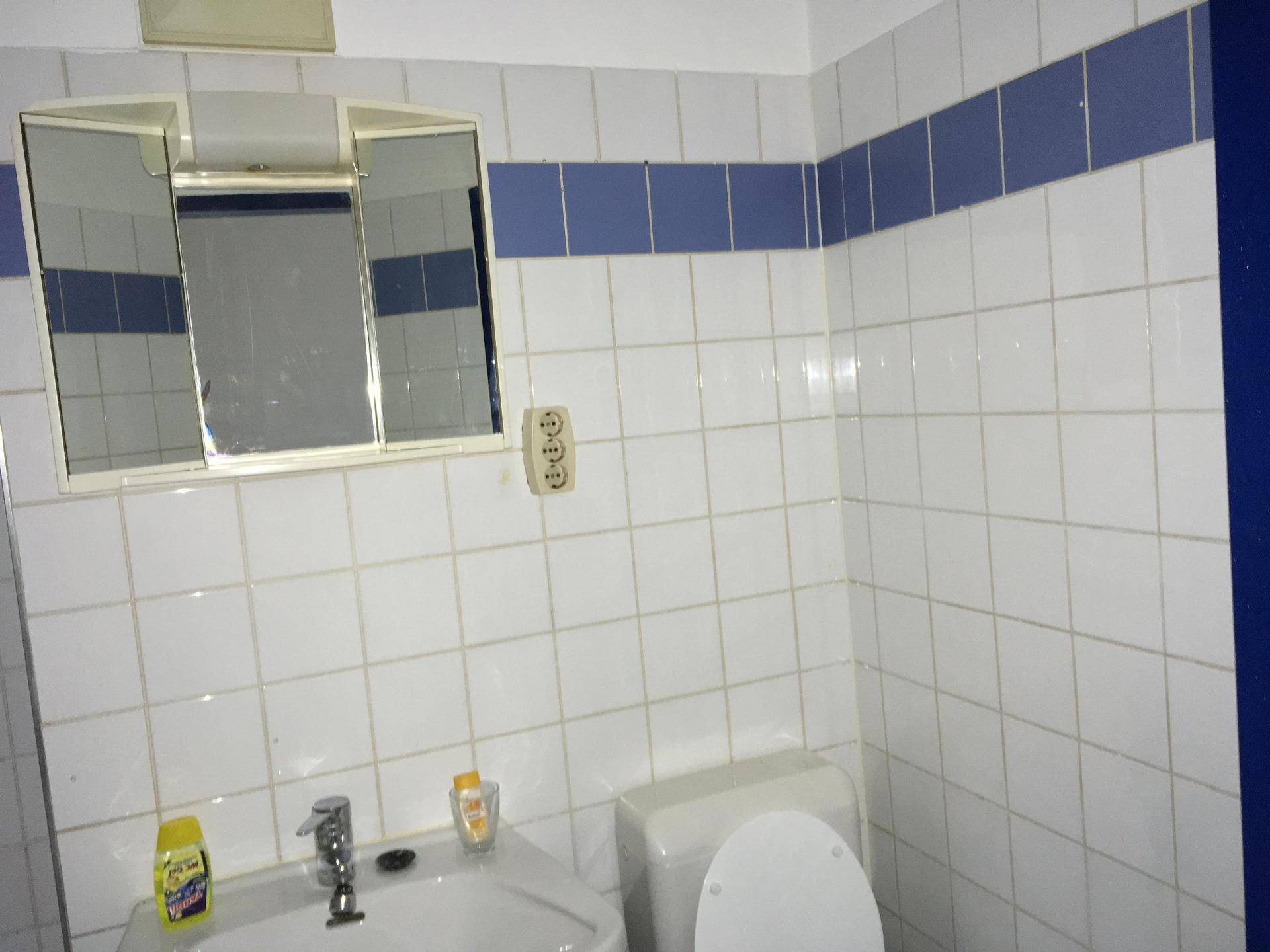 Badezimmer mit weißen Wandfliesen, blauer Akzentleiste, Waschbecken, Toilette und Spiegelschrank.