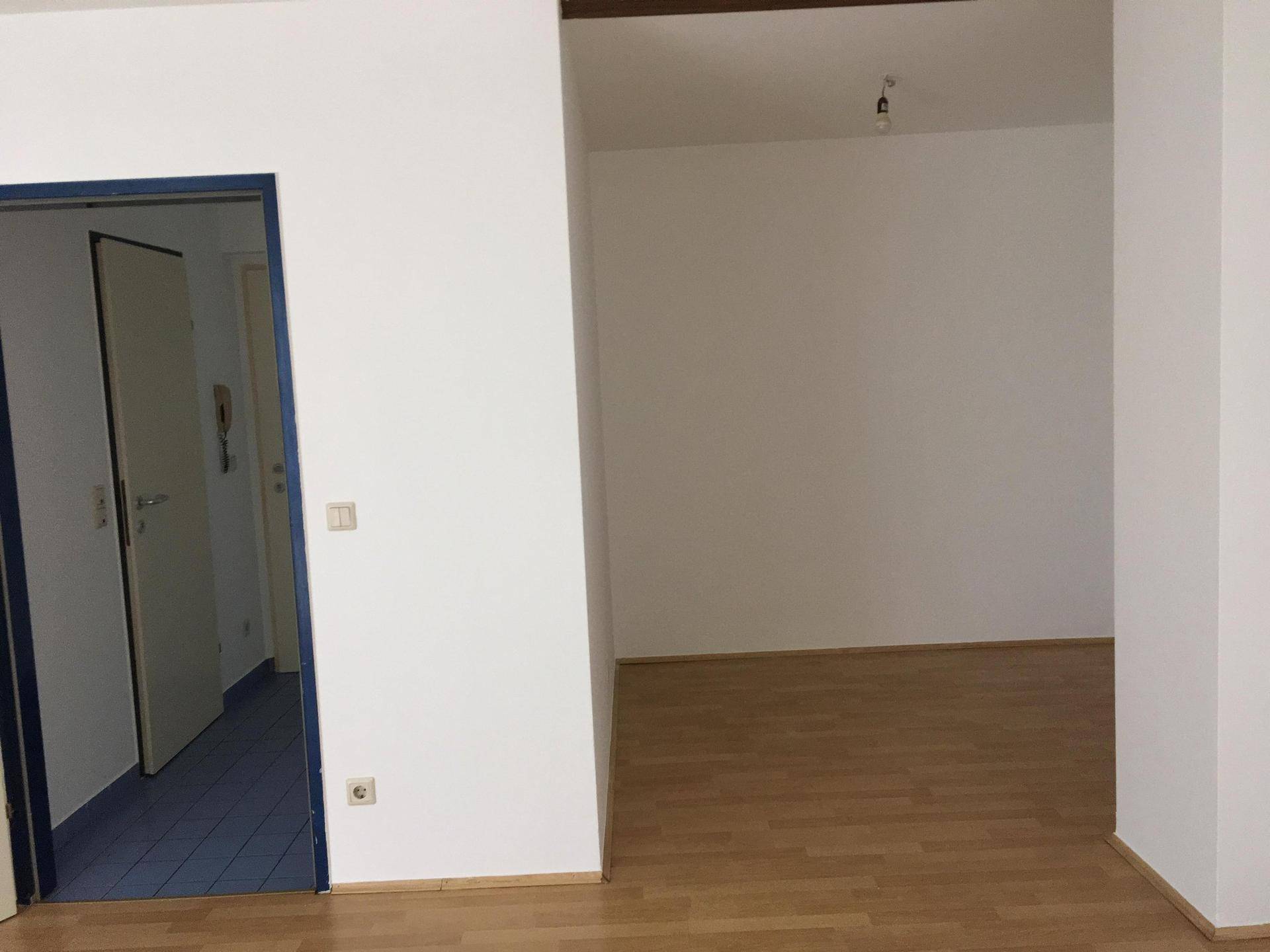 Leerer Raum mit Parkettboden und einem Durchgang zu einem angrenzenden Bereich mit blauen Fliesen.