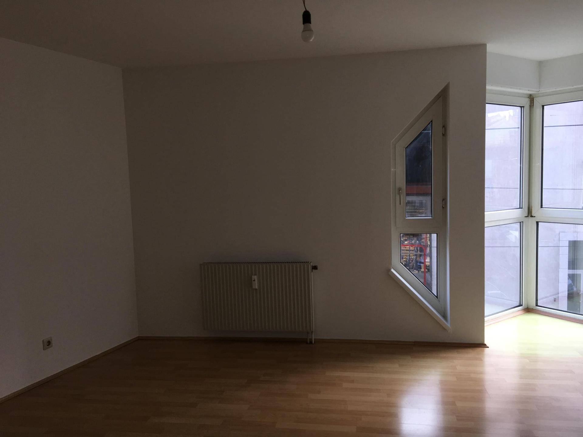 Geräumiger Wohnbereich mit hellem Parkettboden und einer markanten Eckfenstergestaltung für gute Belichtung.