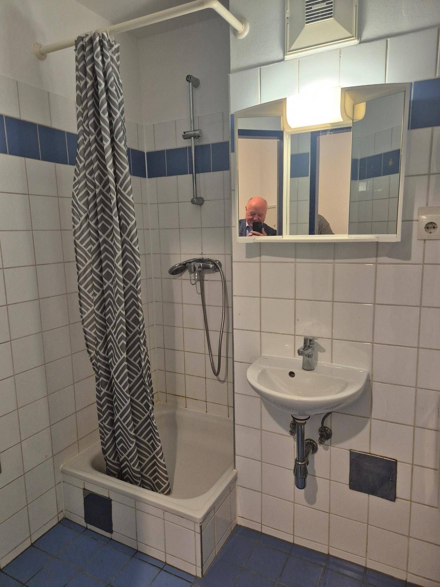 Badezimmer mit Duschbereich, Duschvorhang, Waschbecken und Spiegelschrank, umgeben von weißen und blauen Fliesen.
