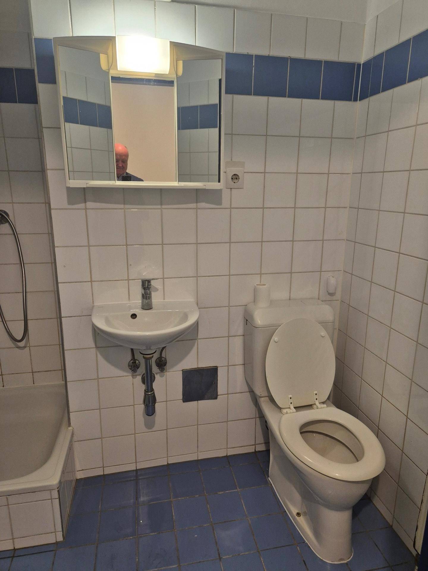 Badezimmer mit weißen und blauen Fliesen, ausgestattet mit Toilette, Waschbecken und Spiegelschrank.