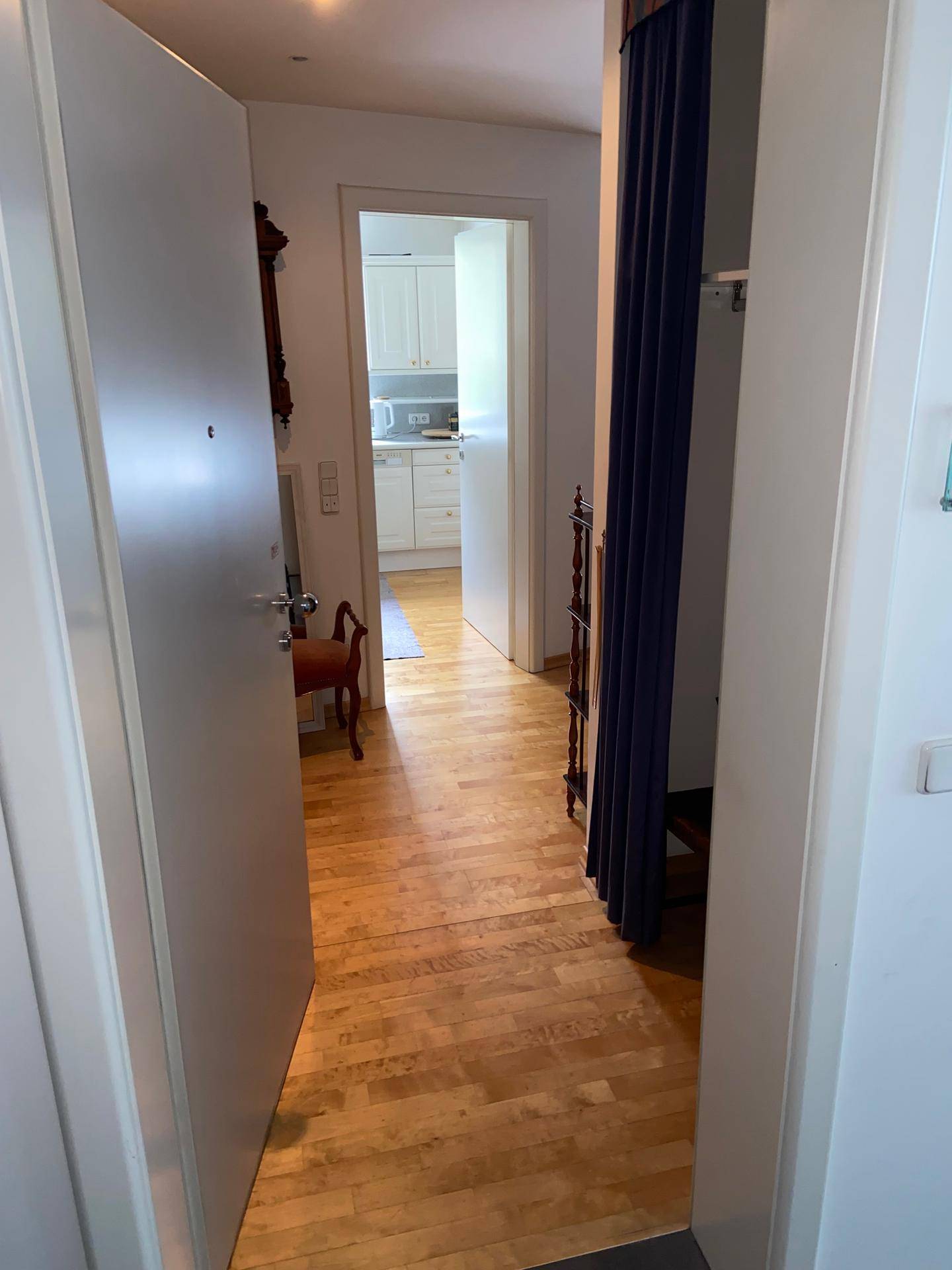Heller Flur mit Parkettboden, der zu einem weiteren Raum führt, mit Blick auf eine weiße Küche im Hintergrund.