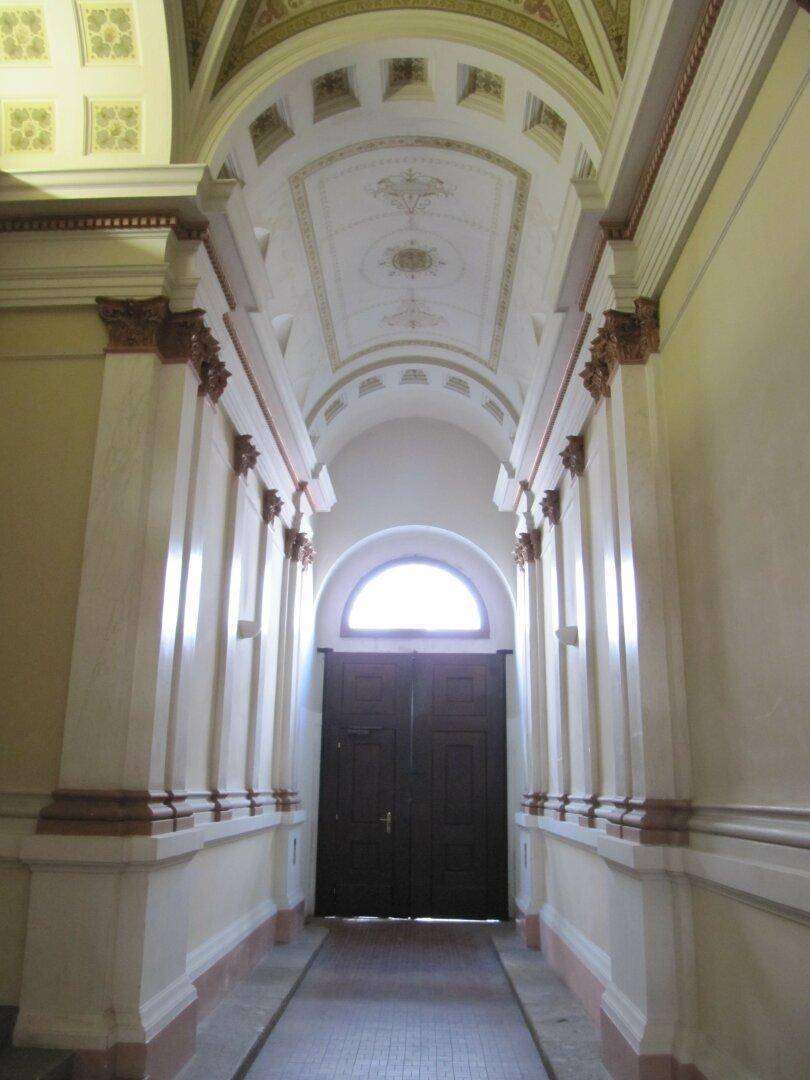 Eindrucksvoller Flur mit kunstvollen Gewölbedecken und einer großen Doppeltür mit Rundbogenfenster.