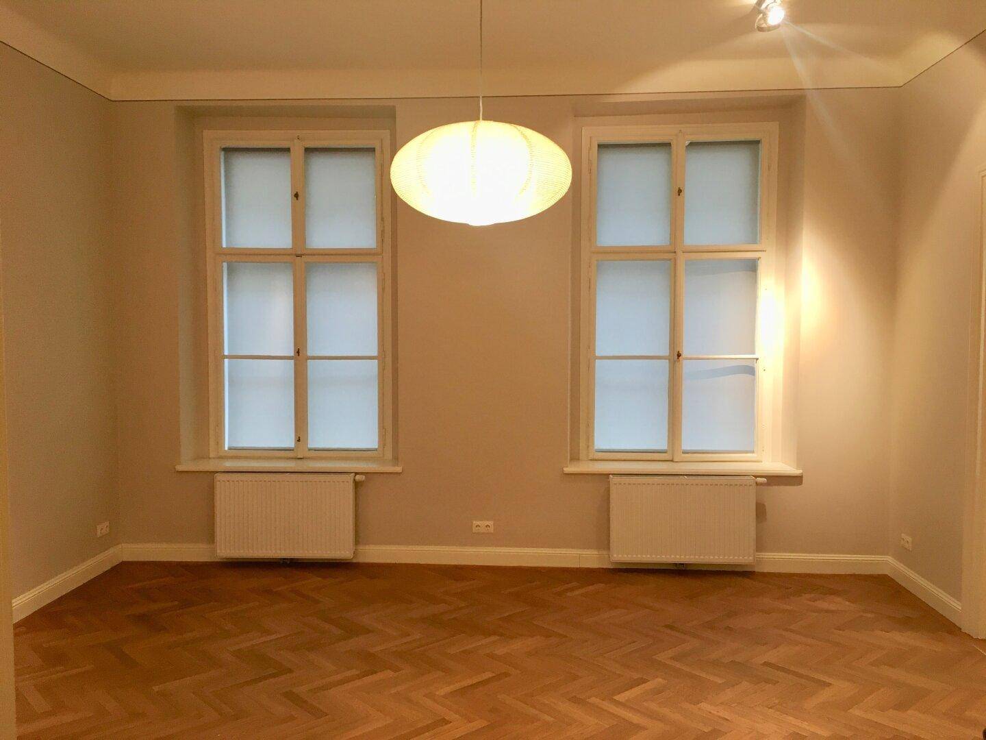 Geräumiger Raum mit großen Fenstern, die viel Tageslicht hereinlassen, und klassischem Parkett.