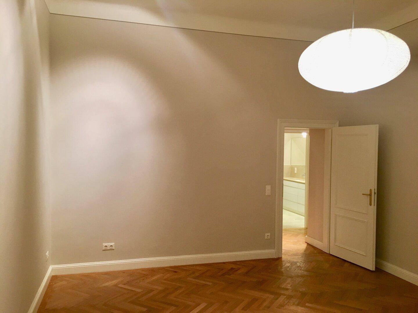 Leeres Zimmer mit Fischgrätparkett und einem Durchgang zu einer modernen Küche.