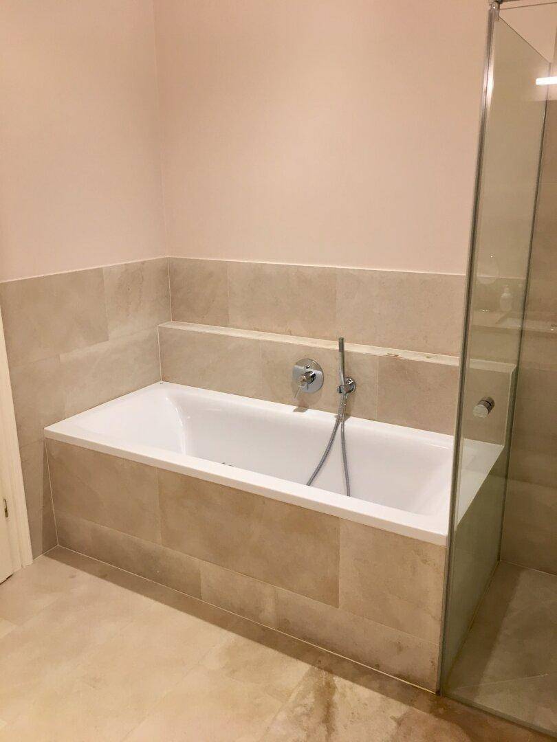 Elegantes Badezimmer mit einer eingebauten Badewanne und hochwertigen beigefarbenen Fliesen.