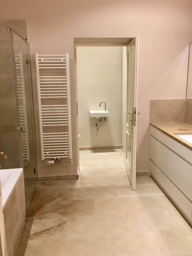 Helles Badezimmer mit Handtuchheizkörper und Zugang zu einer separaten Gästetoilette.
