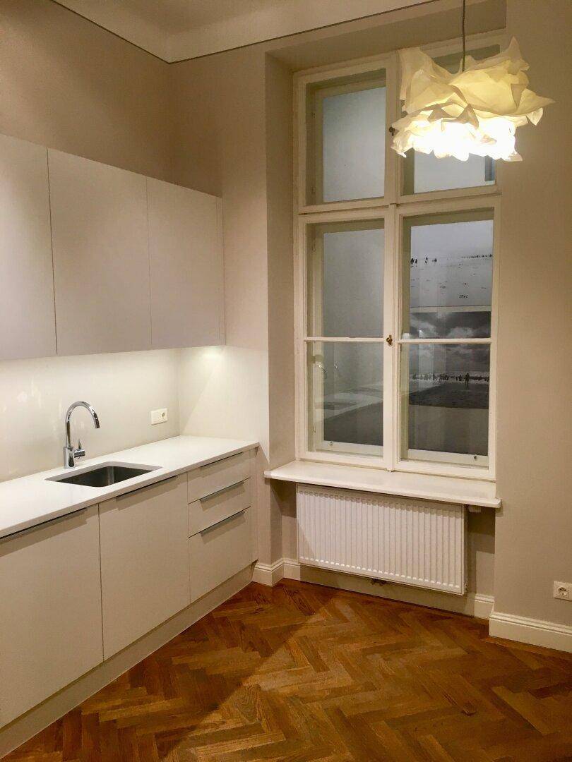 Moderne Küche mit weißen Schränken, Spüle und einem Fenster mit Heizkörper.