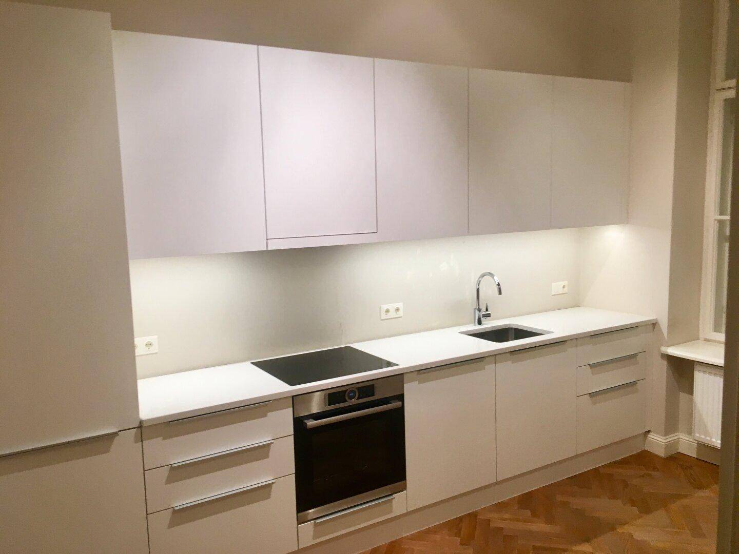 Elegante Küche mit weißen Schränken, Induktionskochfeld und integriertem Backofen.