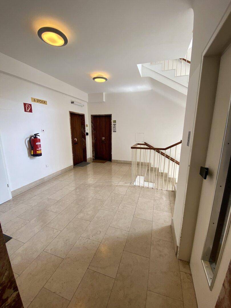 Heller Hausflur mit Treppenhaus, Aufzug und Fliesenboden, der zu den Wohnungen führt.