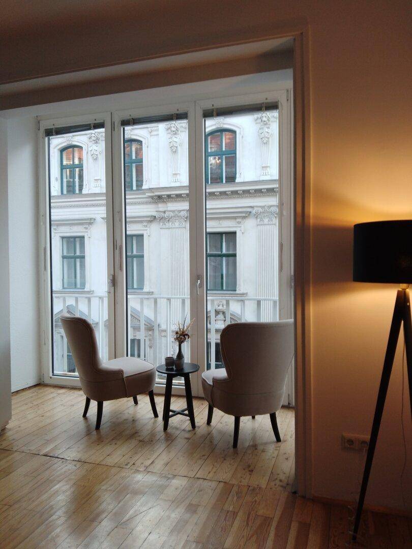 Gemütliche Sitzecke mit zwei Sesseln und einem kleinen Tisch vor großen Fenstern mit Blick auf die Fassade.