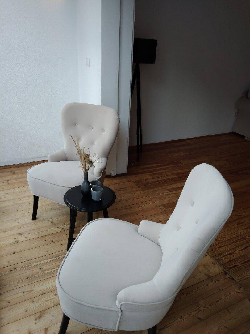 Zwei bequeme Sessel mit einem kleinen Beistelltisch in einem hellen Raum mit Holzboden.