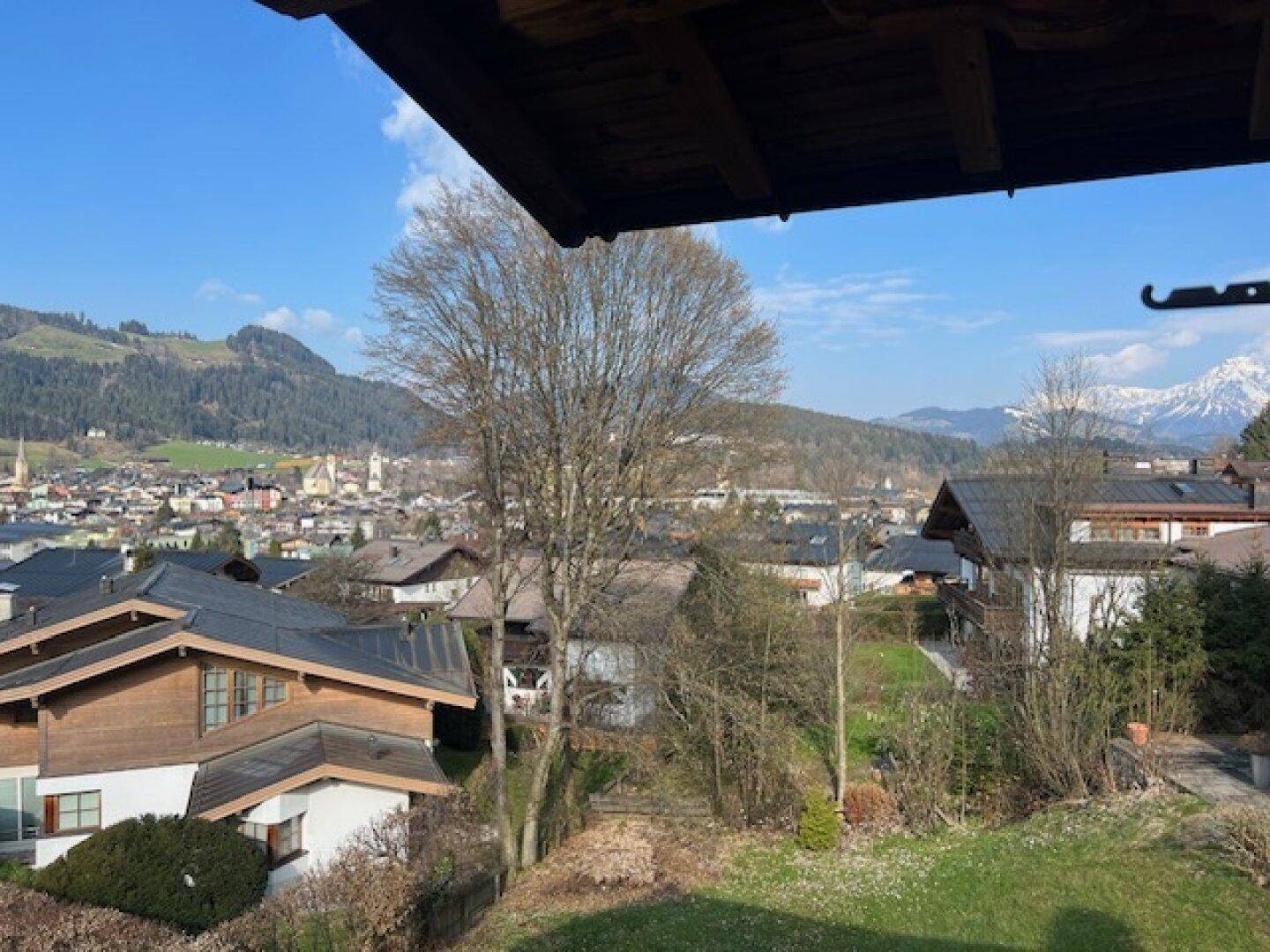 Blick von der Immobilie auf eine Stadt, grüne Hügel und schneebedeckte Berge mit Rasen im Vordergrund.