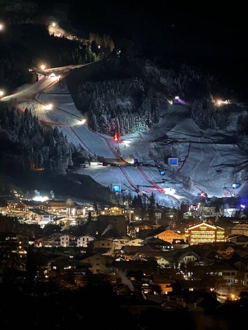 Nachtansicht einer verschneiten Stadt mit hell beleuchteten Skipisten und festlich geschmückten Gebäuden.