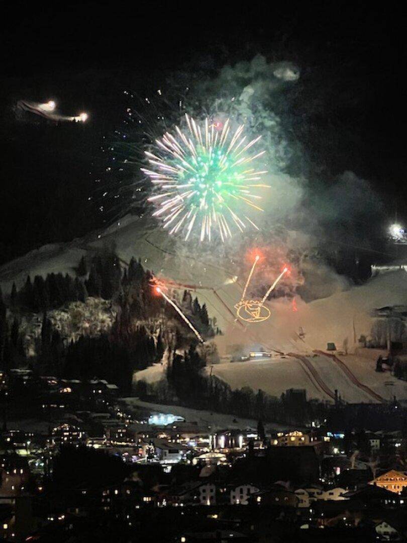 Spektakuläres Feuerwerk über den verschneiten Skipisten und der beleuchteten Stadt bei Nacht.