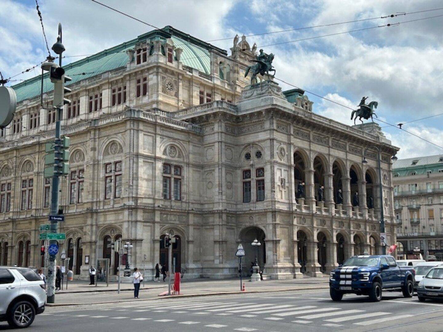 Prächtiges historisches Gebäude mit grüner Kuppel und Statuen an einer belebten Stadtkreuzung.